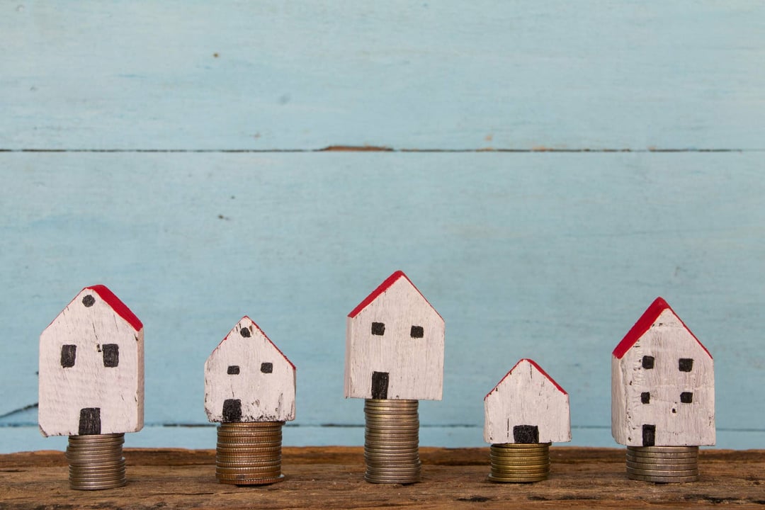 Representation of tax inequality, small wooden homes are stacked on piles of coins reaching different heights